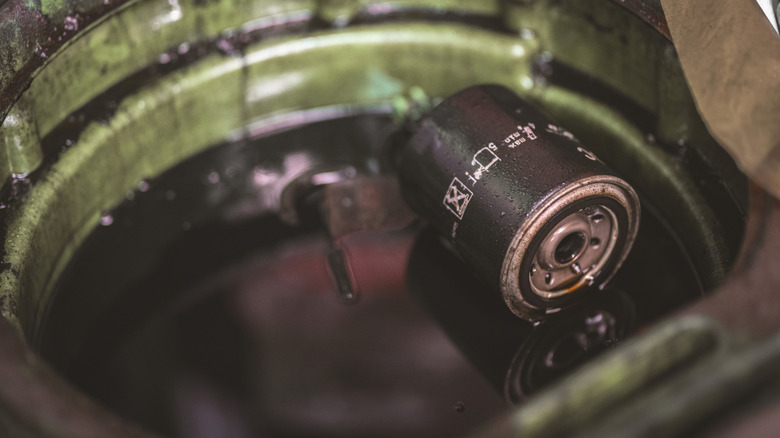Mecânico mostra o filtro de óleo em um motor de carro, destacando a manutenção preventiva.