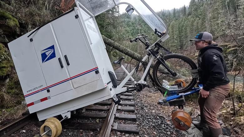 Matt Spears sorrindo enquanto pedala a e-bike camper adaptada sobre trilhos ferroviários.