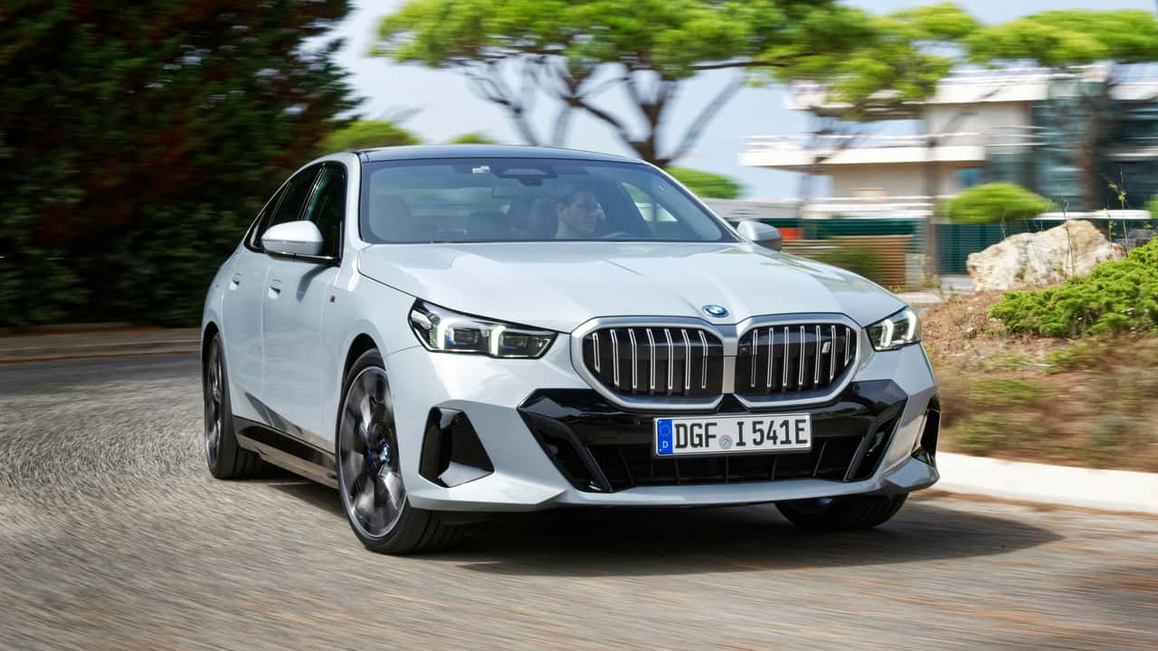 BMW i5 2026 prata em uma estrada de montanha, mostrando o design frontal do sedã elétrico.