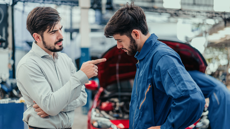 Mecânico mostra peça automotiva a um cliente em uma oficina
