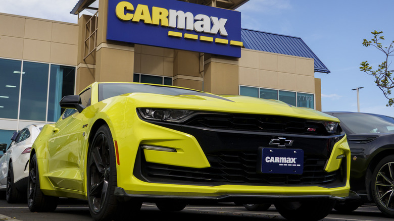 Fachada de uma loja CarMax em um dia ensolarado, com vários carros estacionados no pátio.