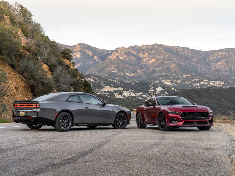 Dodge Charger cinza e Ford Mustang GT vermelho lado a lado em uma estrada