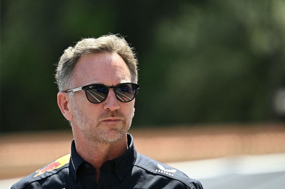 Christian Horner em perfil, com capacete de piloto e fundo desfocado da equipe Red Bull