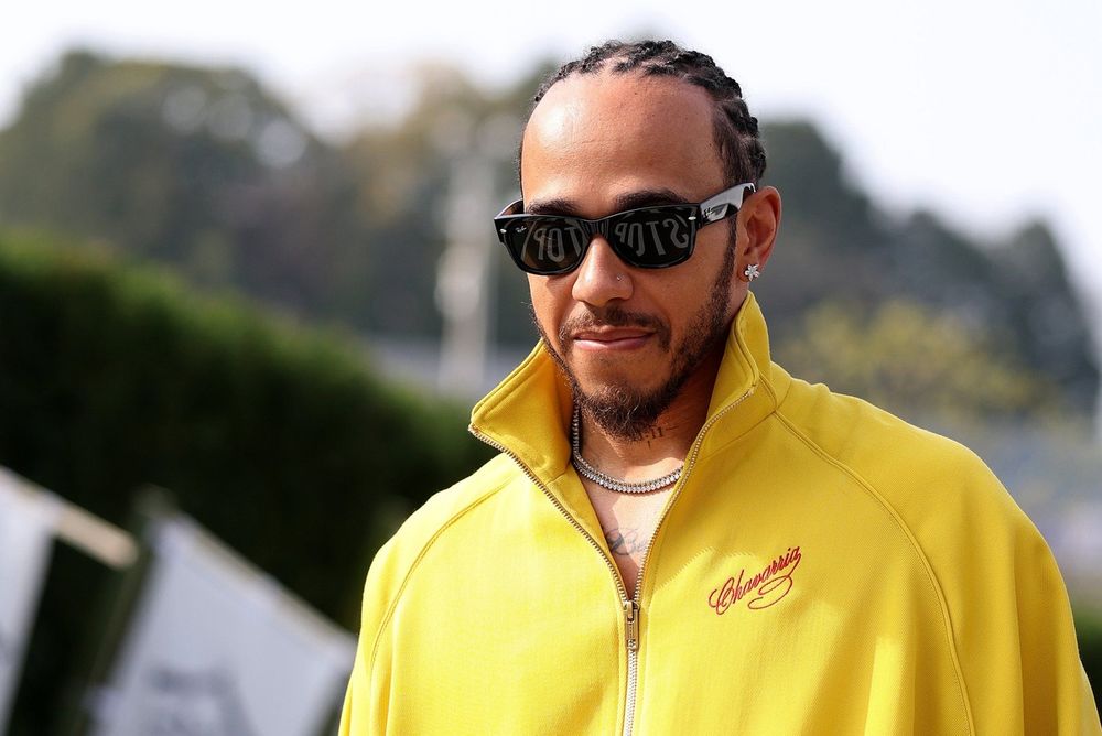 Lewis Hamilton em traje de piloto ao lado de carro de Fórmula 1 da Ferrari