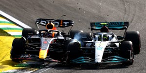 Max Verstappen em uniforme de corrida da Fórmula 1, sorrindo e com o capacete na mão, ao lado de um carro de corrida