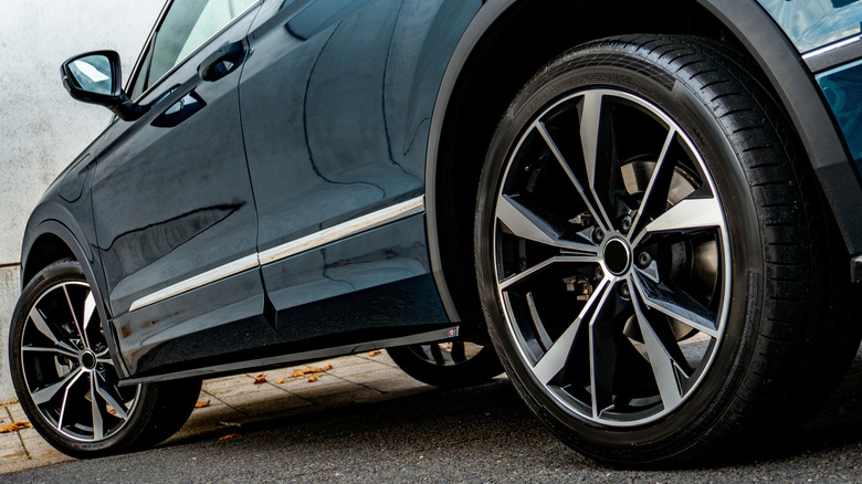 Carro azul esportivo com rodas de liga leve pretas e pinças de freio vermelhas