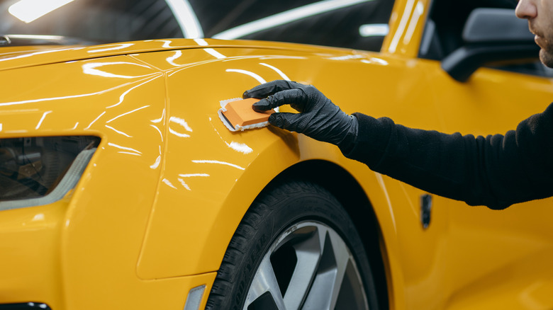 Pessoa detalhando o capô de um carro amarelo com um pano de microfibra, mostrando uma superfície brilhante