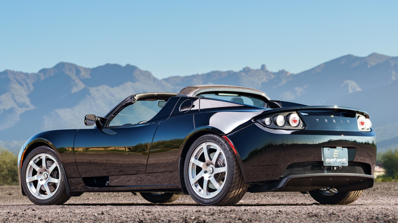 Tesla Roadster original, de cor vermelha, estacionado com as portas abertas, exibindo seu design compacto e esportivo.